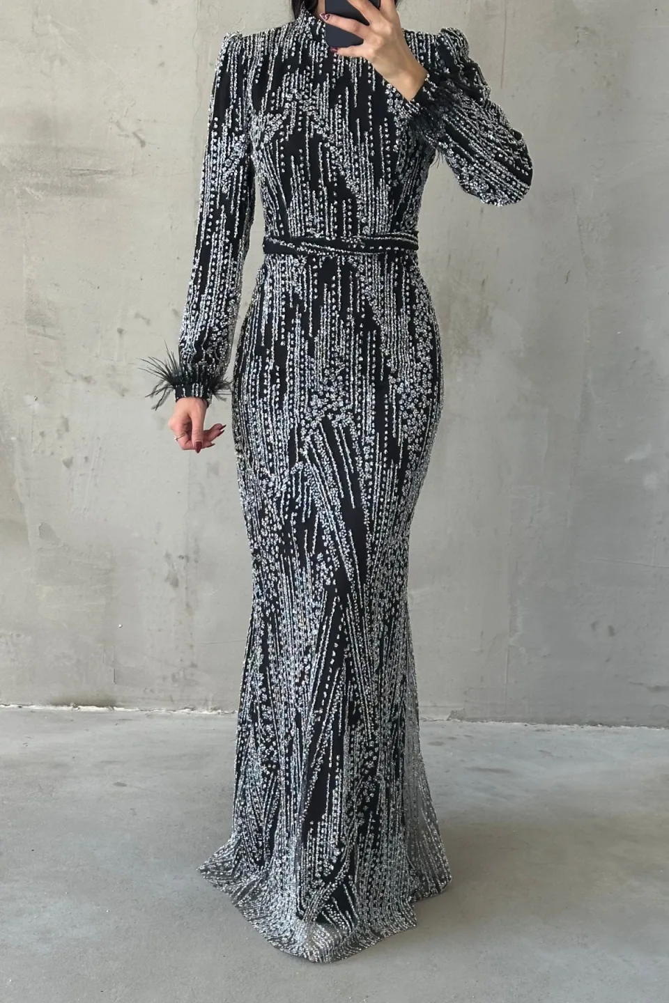 Black sequined maxi dress with long sleeves, belted waist, and feather trim on the cuffs.