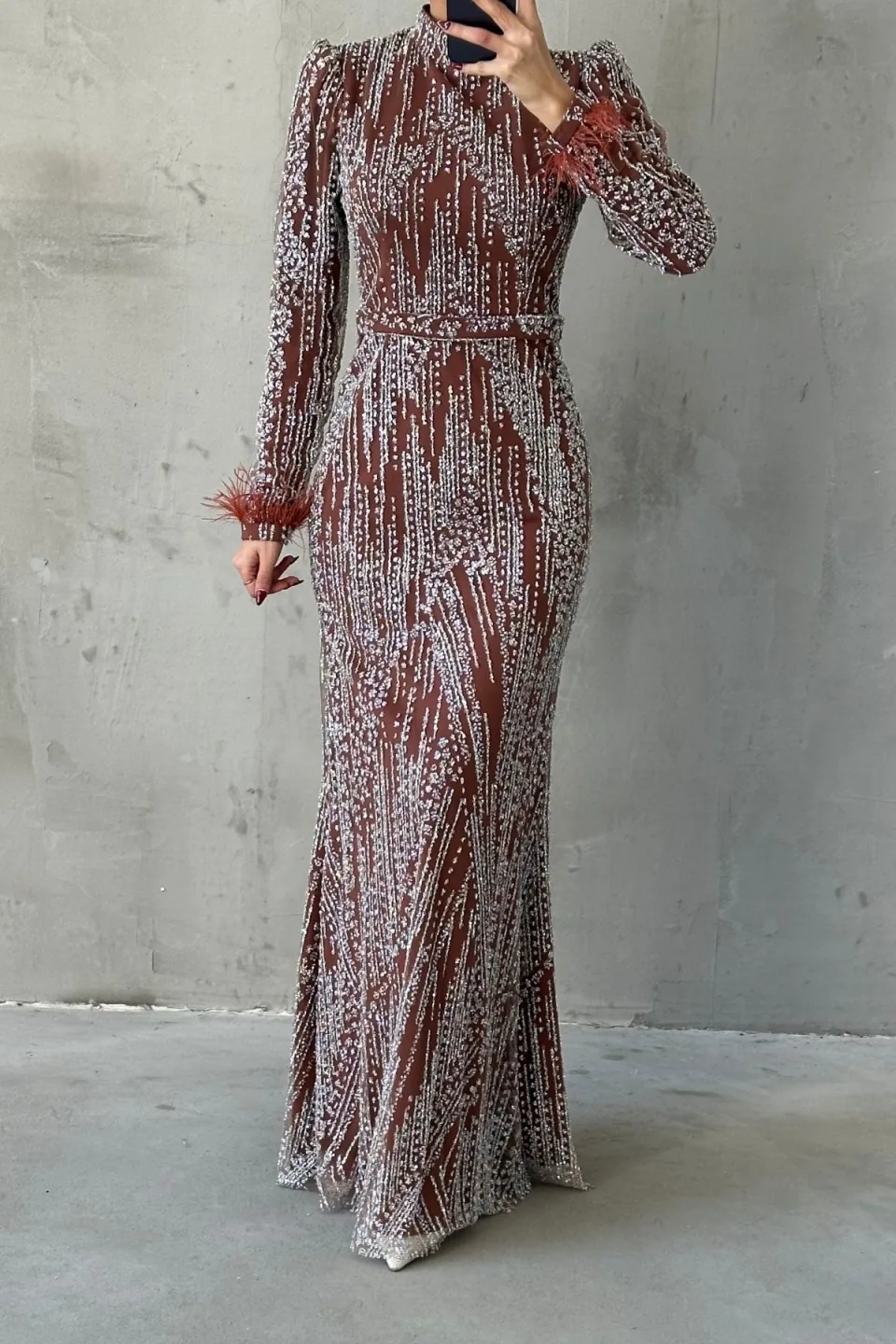 Brown sequined maxi dress with long sleeves, belted waist, and feather trim on the cuffs.