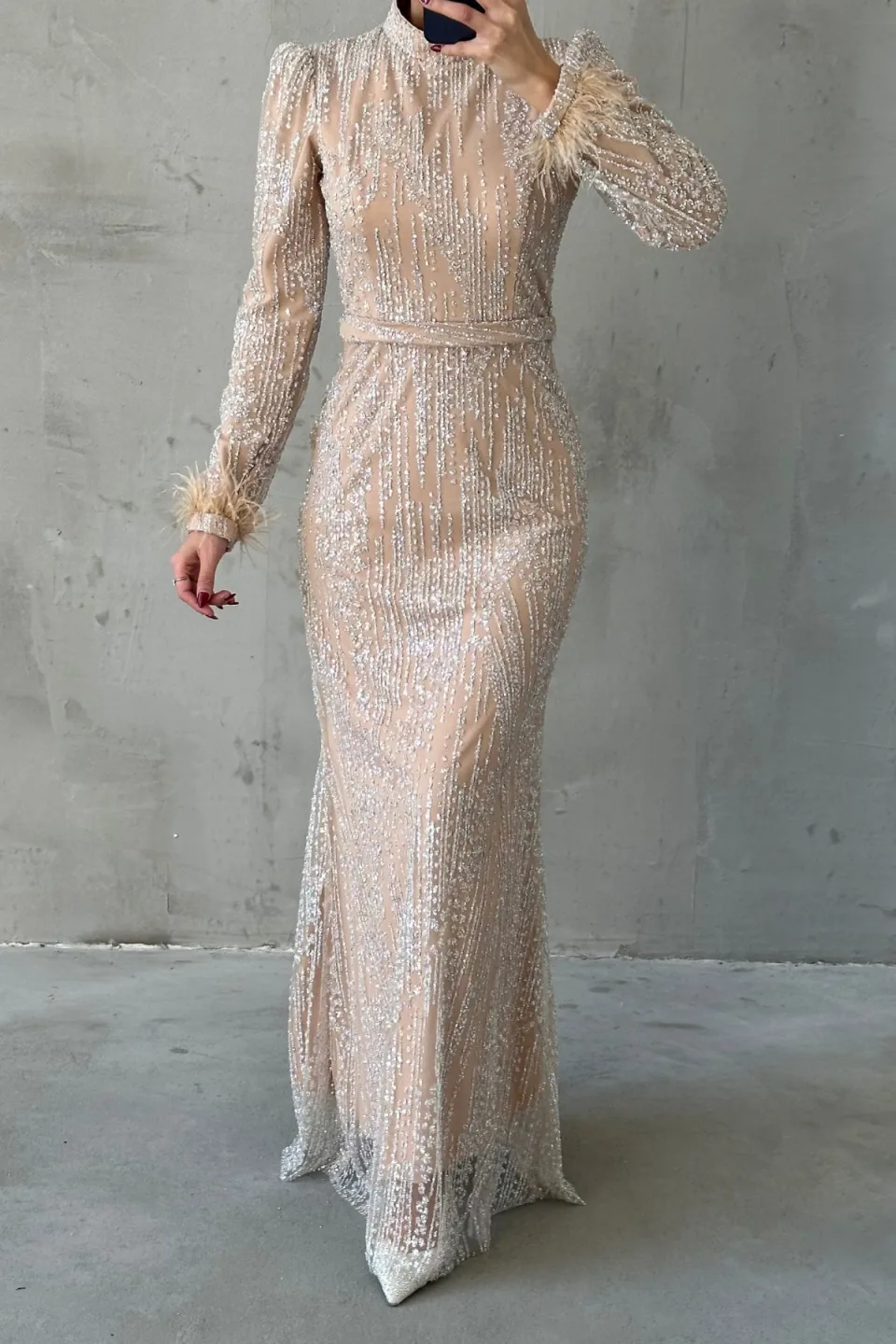 Champagne sequined maxi dress with long sleeves, belted waist, and feather trim on the cuffs.