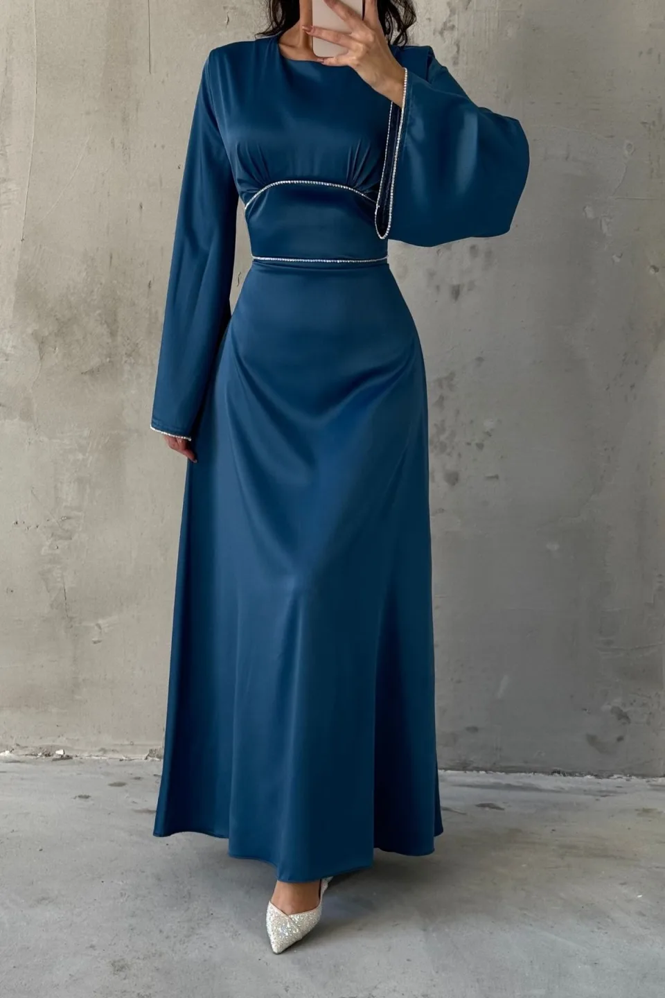 Blue maxi dress with wide, flowing sleeves and contrasting white trim along the neckline, waist, and cuffs. The dress is made of a smooth, draping fabric.