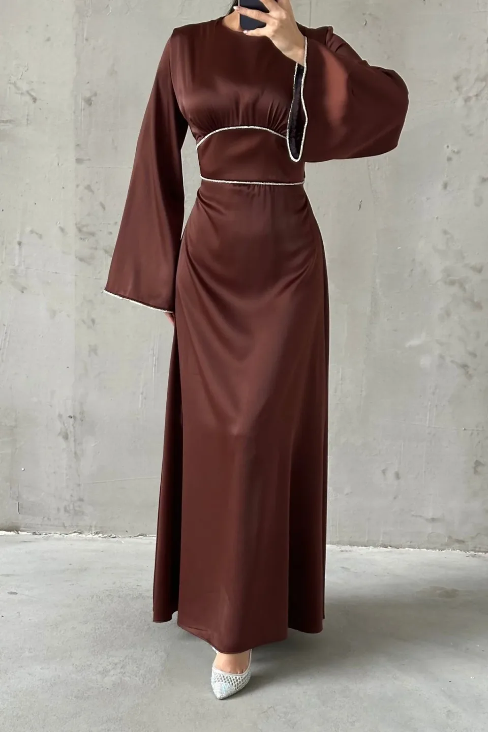 Chocolate brown maxi dress with wide, flowing sleeves and contrasting white trim along the neckline, waist, and cuffs. The dress is made of a smooth, draping fabric.