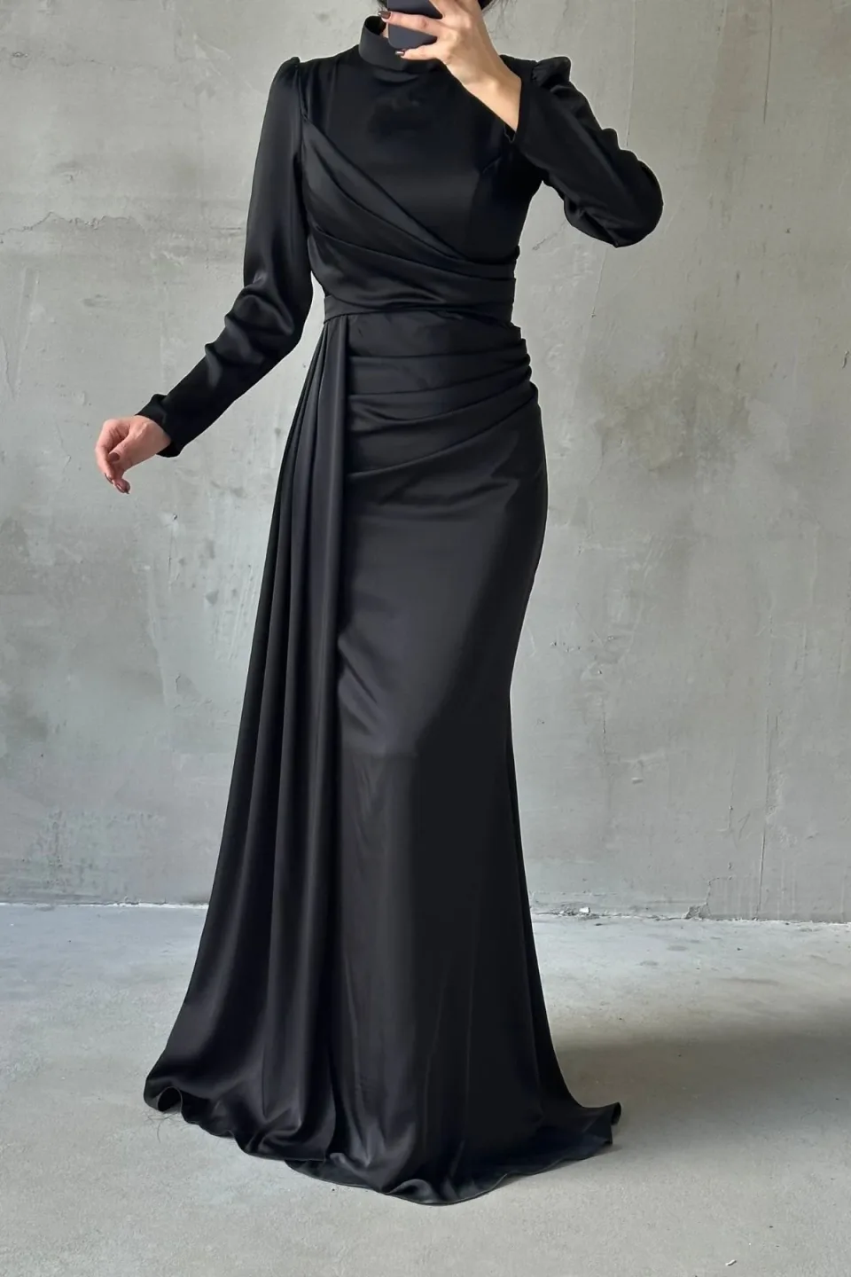 Elegant black formal dress with a flowing tail and refined hijab embellishments. The dress features a long, draped tail and detailed embellishments around the hijab area.