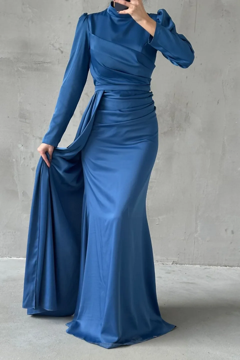 Elegant blue formal dress with a flowing tail and refined hijab embellishments. The dress features a long, draped tail and detailed embellishments around the hijab area.