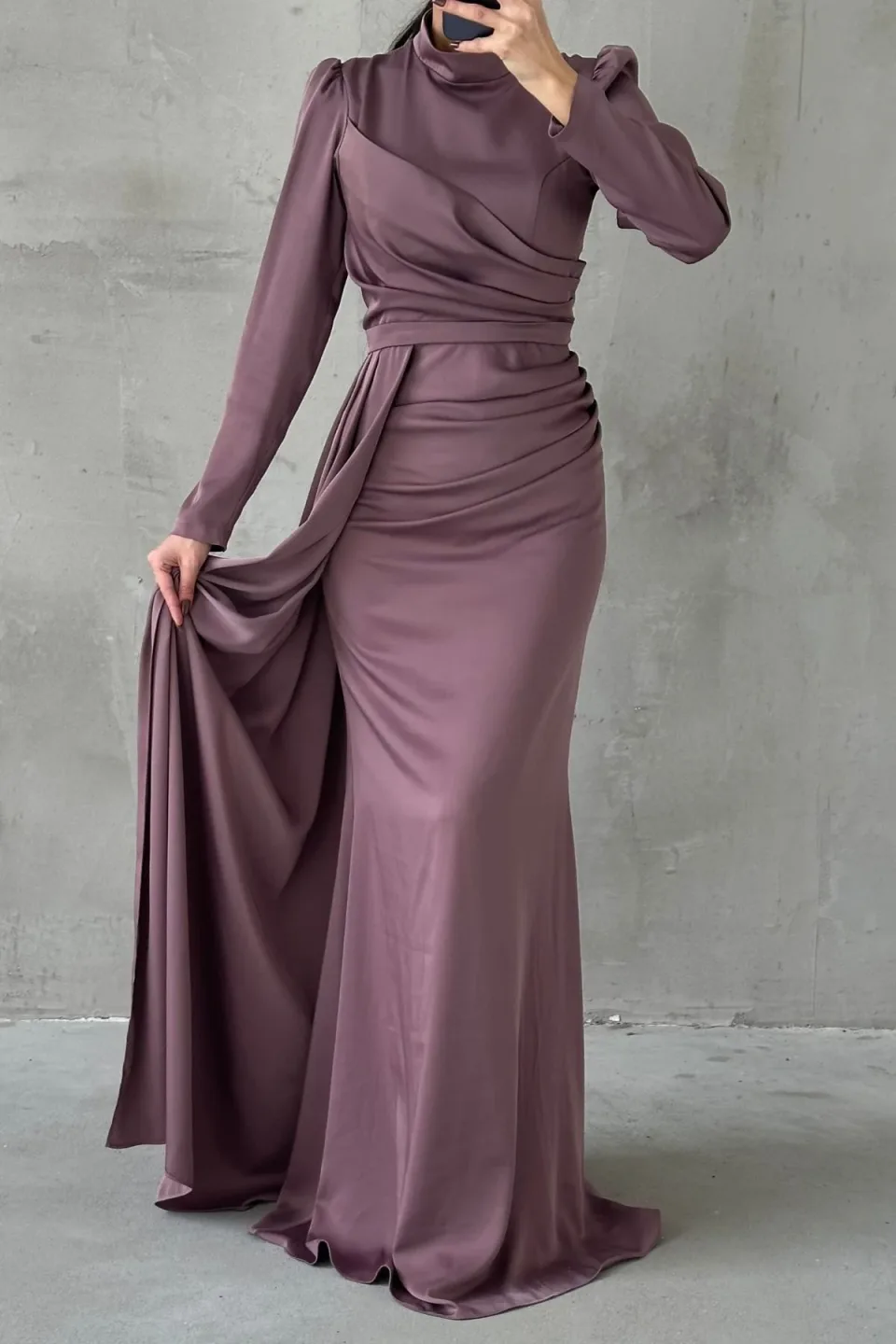 Elegant mauve formal dress with a flowing tail and refined hijab embellishments. The dress features a long, draped tail and detailed embellishments around the hijab area.