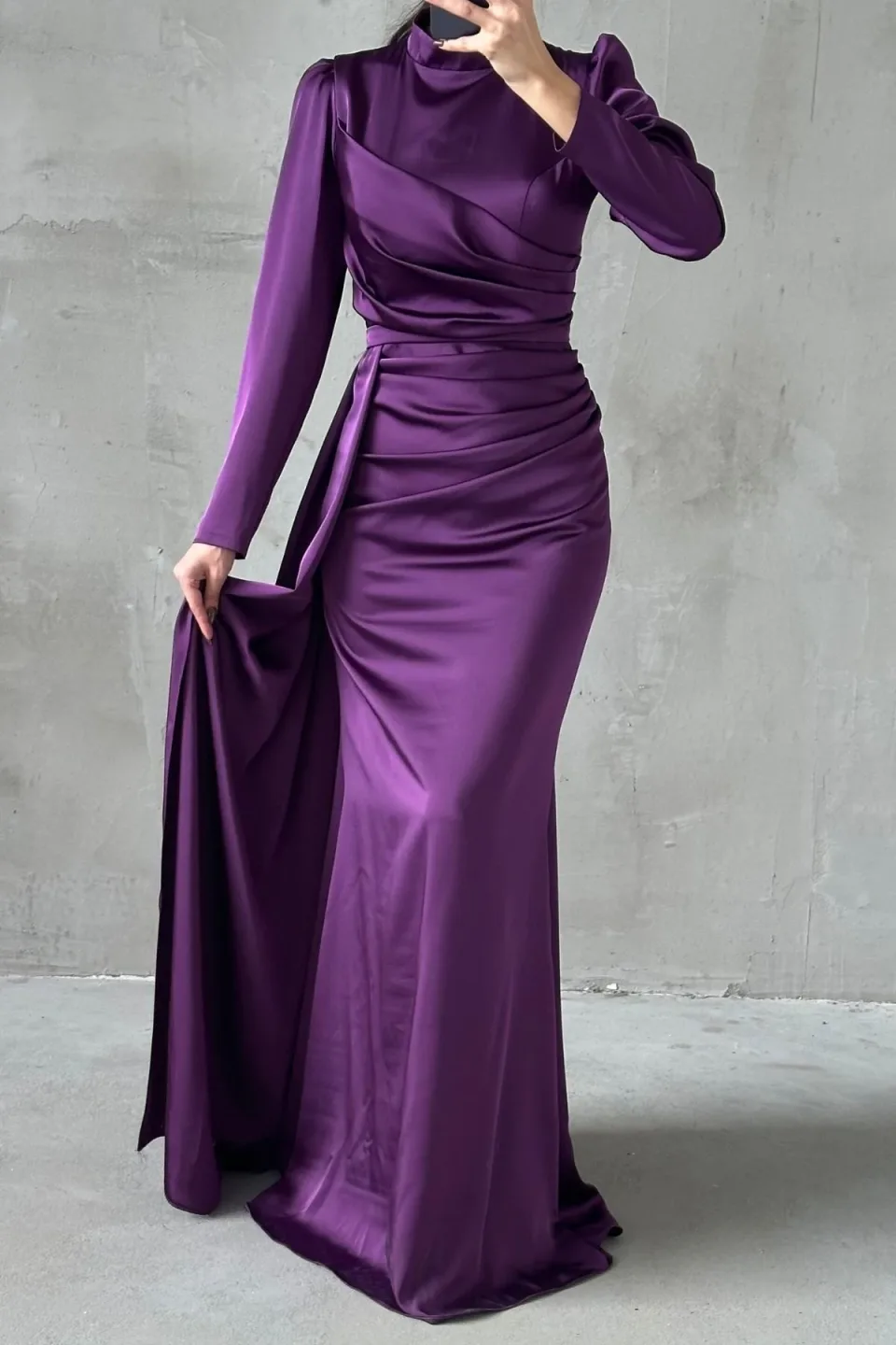 Elegant purple formal dress with a flowing tail and refined hijab embellishments. The dress features a long, draped tail and detailed embellishments around the hijab area.